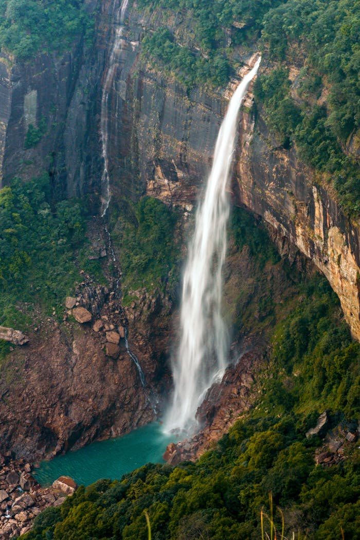 A stunning waterfall cascading down rocky cliffs surrounded by lush green foliage in Meghalaya, India.